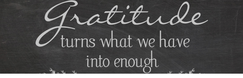Chalkboard sign with the phrase 'Gratitude turns what we have into enough' in elegant cursive lettering and small decorative branches at the bottom.
